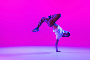 Wall Mural - One young stylish man, break dancing dancer training in modern clothes isolated over bright magenta background at dance hall in neon light.