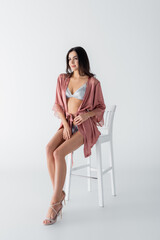 Wall Mural - brunette young woman in sexy underwear and satin robe sitting on chair on white