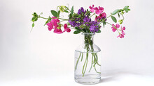 A Bouquet Of Pink And Lilac Wildflowers In A Small Transparent Vase On A White Background