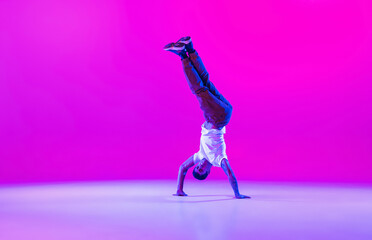 Wall Mural - Young stylish man, hip-hop dancer dancing solo in modern clothes isolated over bright magenta background at dance hall in neon light.