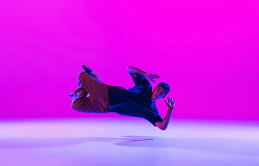 Wall Mural - Young stylish man, break dancing dancer practicing solo in modern clothes isolated over bright magenta background at dance hall in neon light.