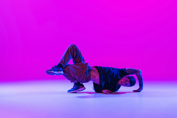 Wall Mural - Modern dance style. Hip hop, break dancing dancer in action, motion in dark clothes isolated over bright magenta background at dance hall in neon light.