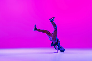 Wall Mural - Young stylish man, hip-hop dancer dancing solo in modern clothes isolated over bright magenta background at dance hall in neon light.