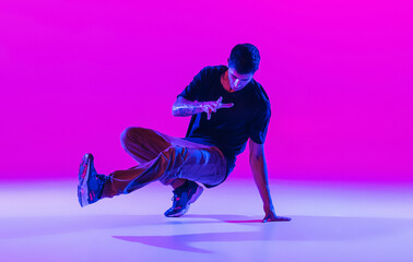 Wall Mural - Portrait of dancing man, break dancer in action, motion in modern clothes isolated over bright magenta background at dance hall in neon light.