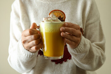 Woman in sweater holds glass of pumpkin latte