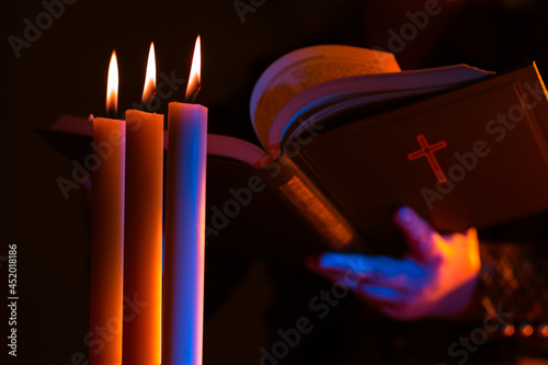 Woman reads Bible by the light of three candles. Christianity concept. Protestantism, Catholicism and Orthodoxy. Catholic woman communicates with God. Reading religious literature. Faith in God.