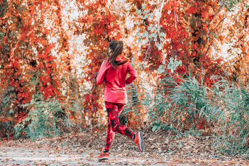 Wall Mural - Running woman jogging on autumn red leaves foliage background. Fall cardio exercise training. Happy athlete runner exercising outdoor.