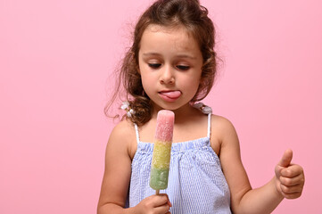 Headshot 4 years pretty baby girl with healthy vegan ice cream popsicle in hand and showing thumb up.Pink background, copy space . Summer dessert, cheerful summer mood concept