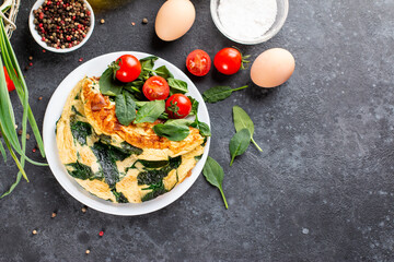 Wall Mural - Omelet with spinach leaves. Omelette on plate, scrambled eggs on a dark slate or concrete background. Top view. Copy space.