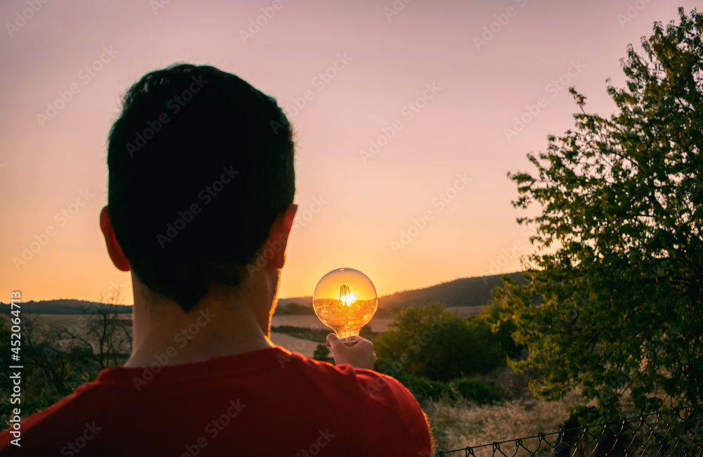 Man holding a light bulb during a sunset - obrazy, fototapety, plakaty 
