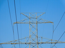 Centered Top Of Powerline Tower With Powerlines Against Clear Sky In Direct Evening Sunlight.