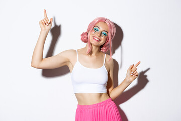 Portrait of happy beautiful girl having fun, dancing and smiling, celebrating holiday on party, wearing pink wig with bright makeup