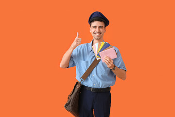 Wall Mural - Handsome young postman with letters showing thumb-up on color background