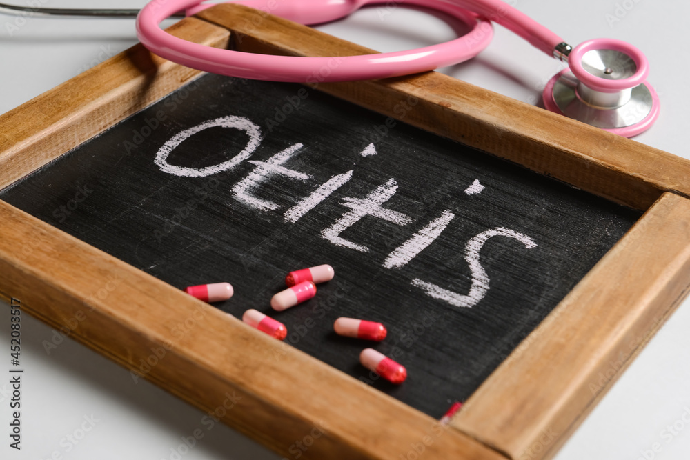Board with word OTITIS, stethoscope and pills on light background