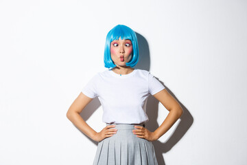 Image of joyful pretty asian girl showing funny faces, squinting and sticking tongue, celebrating halloween at party, standing over white background