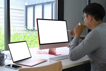 Fototapete - Side view Asian man drinking coffee and working with modern devices.