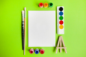 Wall Mural - various painting supplies and blank white canvas on a green background. flat lay. top view. copy space. back to school.