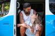 Young tattooed couple laugh and look each other sitting in the side of the van.