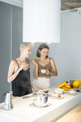 Wall Mural - Lesbian couple have a breakfast together with avocado sandwich and coffee at modern kitchen. Homosexual relations and healthy eating in a comfortable home