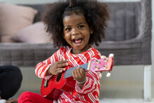 Cheerful African American Little Girl Playing Ukulele Or Small Guitar. Happy Black Little Girl Having Fun With Guitar Or Ukulele. Christmas Holiday Celebration, Merry Christmas, Happy And Holiday