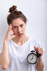 Sleepy young woman keeping alarm clock late for deadline stressed isolated on white color background. Caucasian lady in casual t-shirt look at camera frustrated, tired and exhausted. Copy space