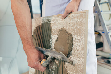 Male worker professional mounts ceramic tile in bathroom photo with close spatula with glue