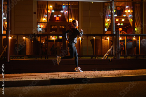 side view on sportive caucasian athlete female running past city cafe at night, sport outdoors. focused motivated woman is running forward, leading active and healthy lifestyle, cardio training