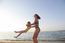 Mother And Daughter Having Fun On The Beach. Mother Holding Girls Hands And Spinning Around. Family Outdoor Activities Concept.