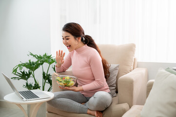 Wall Mural - Portrait of colombian housewife watching movie on laptop and eating vegetable salad at home