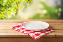 Empty White Plate On Wooden Table With Red Checked Tablecloth Over  Blurred Nature Background.  Kitchen Mock Up For Design And Product Display.