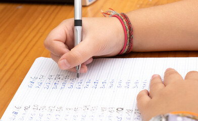 Closeup shot of a little girl's hand writing the multiplication tables in the notebook