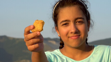 Portrait of a teenage girl. The child holds a nugget in his hand. Sits on the seashore. Dark skin. Rest at the sea. People on the street. Close-up.