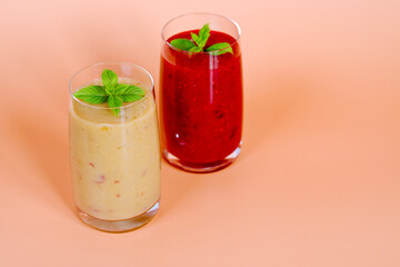 Top view of two different fresh healthy smoothies in a glasses made of peach, banana and berries with mint. Creative concept of healthy detox drink, diet or vegetarian food concept. Copy space.