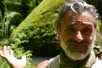 Wall Mural - Mid-aged male showing a big piece of rock with moss in the background over lake water on sunny day