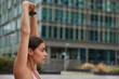 © wayhome.studio - Profile shot of sporty woman raises arms warms up before workout wears smartwatch focused into distance poses against blurred background has regular training. People and healthy lifestyle concept