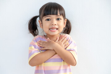 Close up of cute happy small girl isolated on white background hold hands at heart chest feel grateful, smiling little child with eyes closed pray thanking god high powers, faith concept