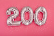 From above of silver shiny balloons demonstrating number 200 on pink background with scattered glitter