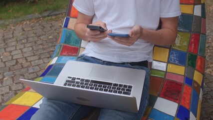 Poster - Two phones in the hands of the user. Laptop on your lap. Man uses the phone on courtyard of the house. Hands typing text on the keyboard. Focus of attention to the monitor.