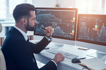 Canvas Print - Concentrated young man in shirt and tie analyzing data on the stock market while working in the office