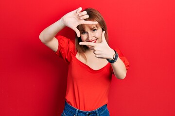 Poster - Redhead young woman wearing casual red t shirt smiling making frame with hands and fingers with happy face. creativity and photography concept.