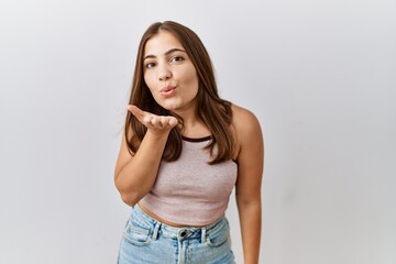 Canvas Print - Young brunette woman standing over isolated background looking at the camera blowing a kiss with hand on air being lovely and sexy. love expression.