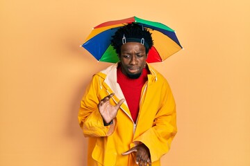 Sticker - Young african american man wearing yellow raincoat disgusted expression, displeased and fearful doing disgust face because aversion reaction.