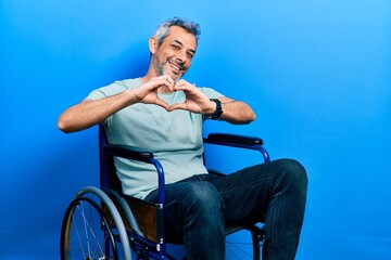 Poster - Handsome middle age man with grey hair sitting on wheelchair smiling in love doing heart symbol shape with hands. romantic concept.