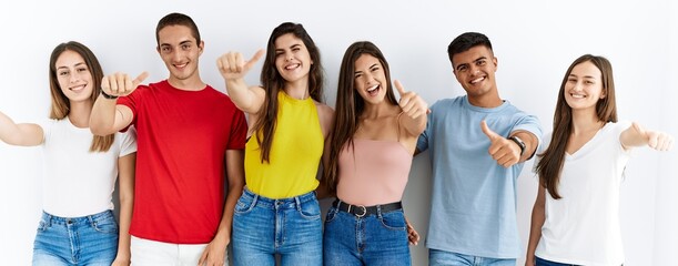 Sticker - Group of people wearing casual clothes standing over isolated background approving doing positive gesture with hand, thumbs up smiling and happy for success. winner gesture.