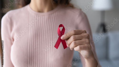 Close up view female volunteer holding red ribbon in hands. Symbol of fighting against HIV, showing support to people with AIDS, concept of awareness, regular medical check up promotion, healthcare