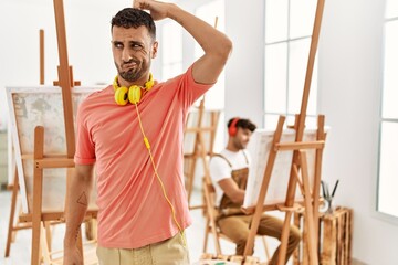 Wall Mural - Young hispanic man at art studio confuse and wonder about question. uncertain with doubt, thinking with hand on head. pensive concept.