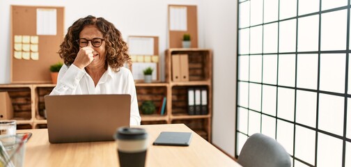 Sticker - Middle age hispanic woman working at the office wearing glasses smelling something stinky and disgusting, intolerable smell, holding breath with fingers on nose. bad smell