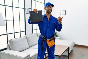 Canvas Print - Young indian technician holding toolbox and screwdriver at house pointing thumb up to the side smiling happy with open mouth