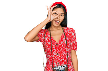 Poster - Beautiful young asian woman wearing dress and vintage camera smiling happy doing ok sign with hand on eye looking through fingers