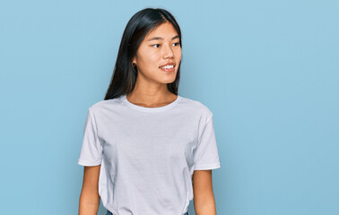 Poster - Beautiful young asian woman wearing casual white t shirt looking away to side with smile on face, natural expression. laughing confident.